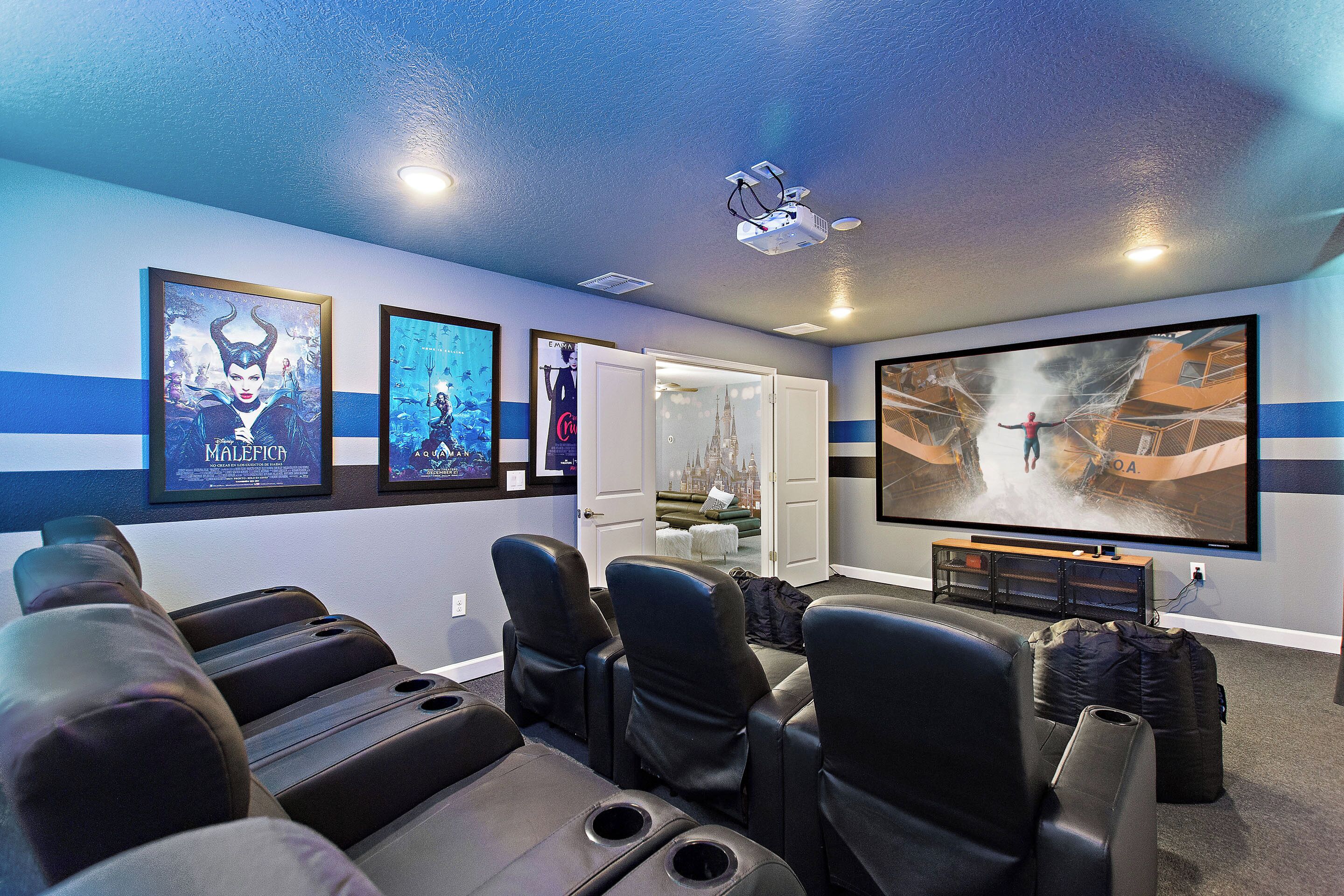 Une salle de cinéma privée équipée d’un grand écran, de fauteuils inclinables et de posters de films accrochés aux murs.