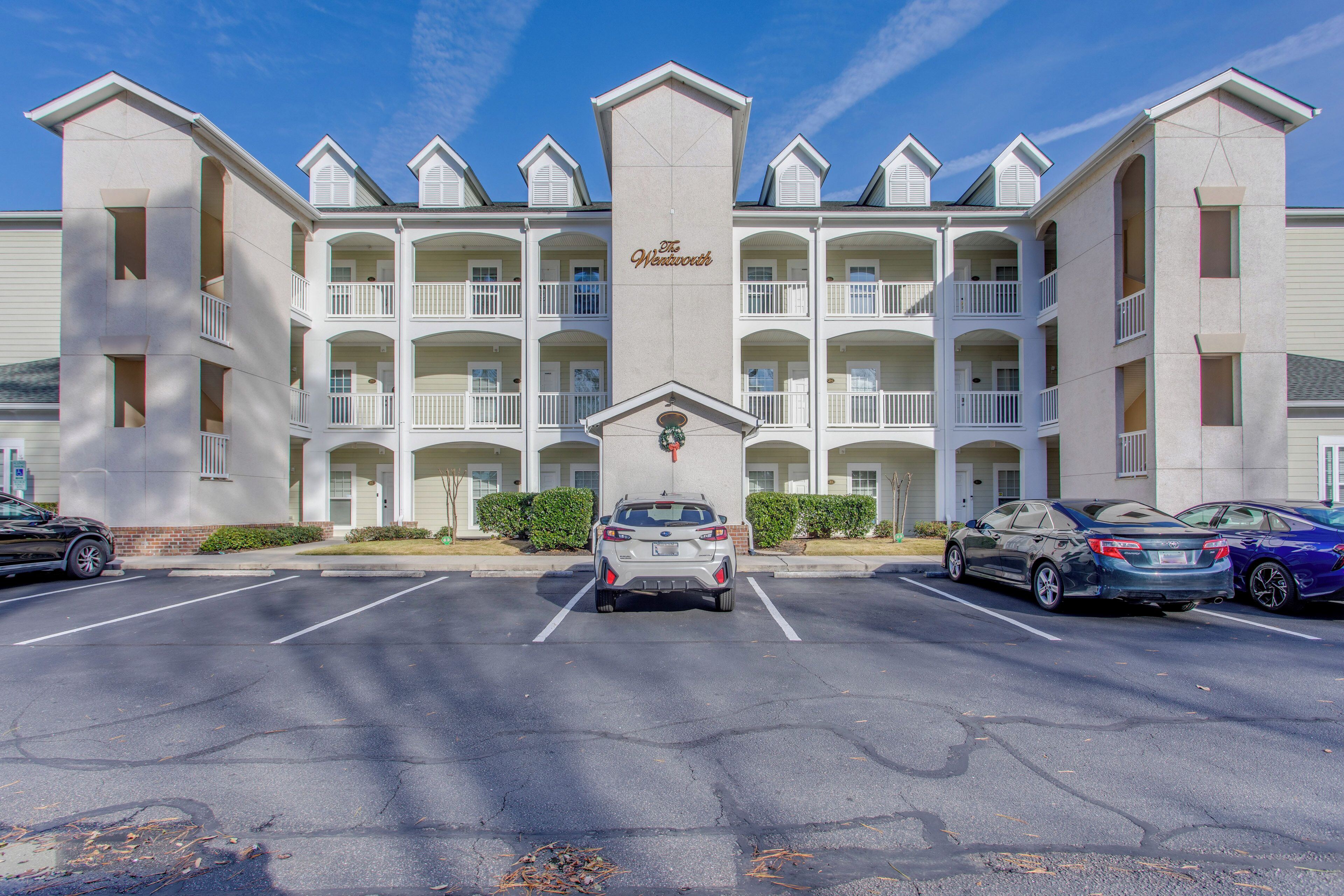 A multi-story hotel with a central entrance, parking lot, and several cars parked in front.