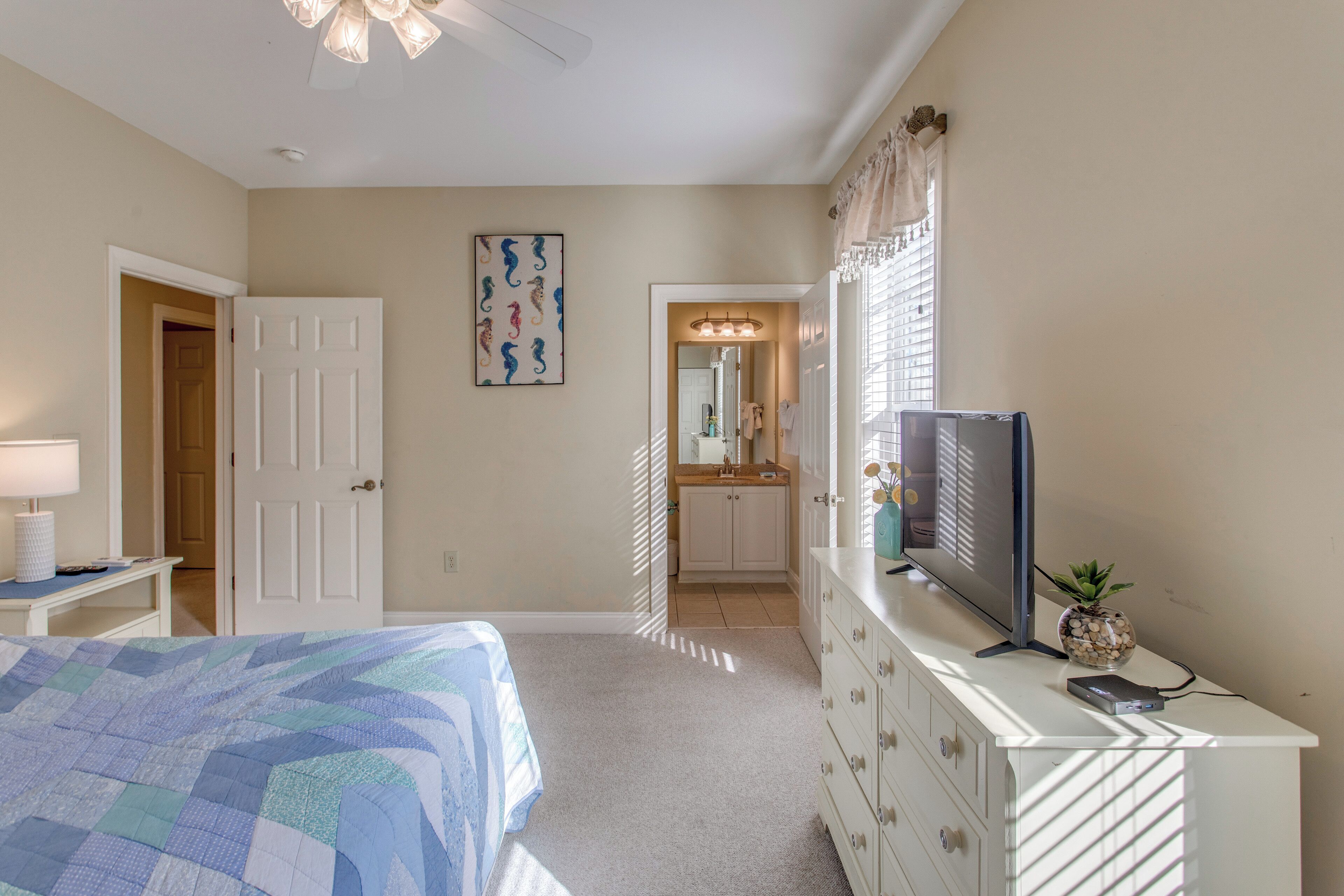 A bedroom with a bed, dresser, TV, and a bathroom visible through an open door.