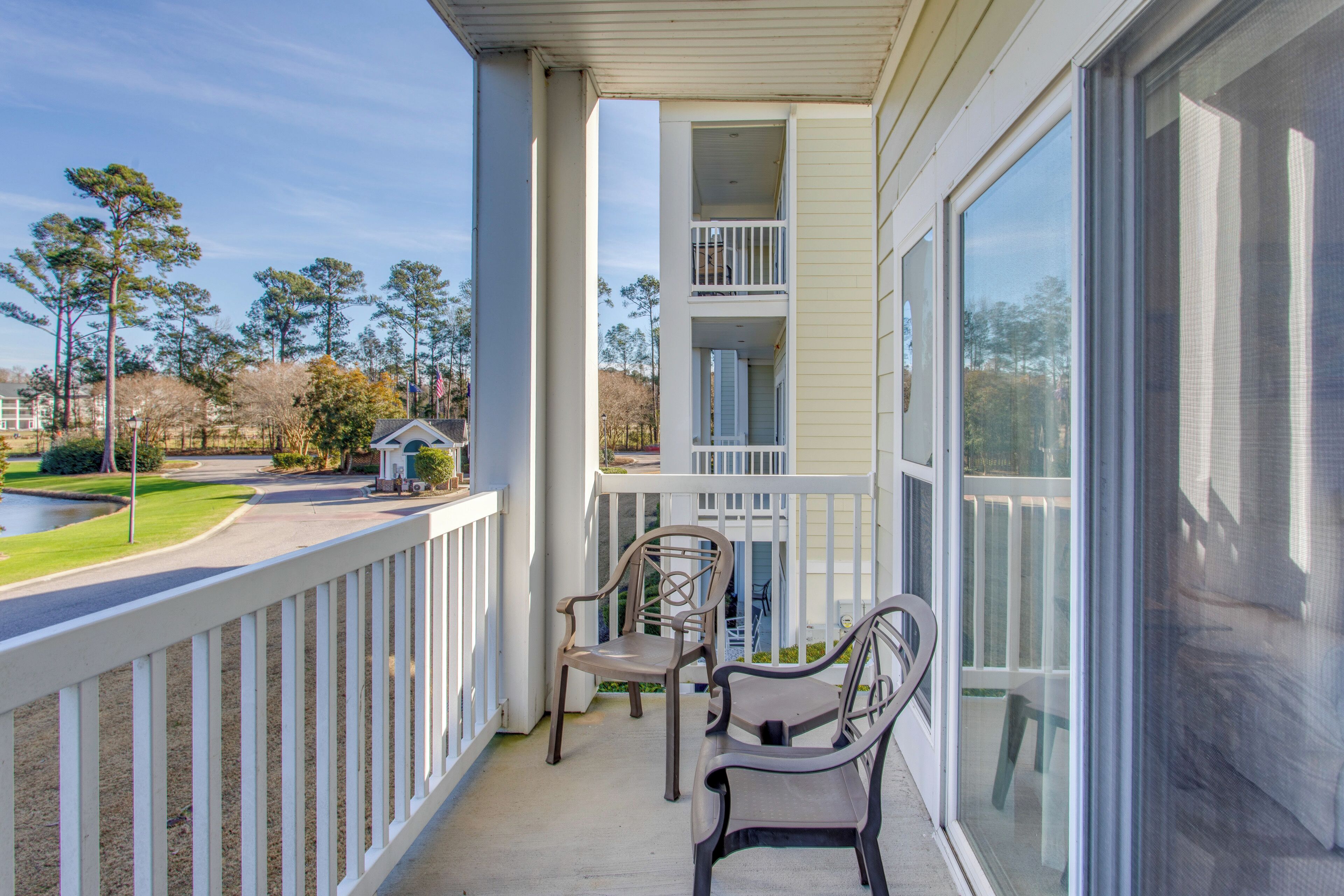 A balcony with two chairs and a small table, overlooking a golf course and a building with a white exterior.