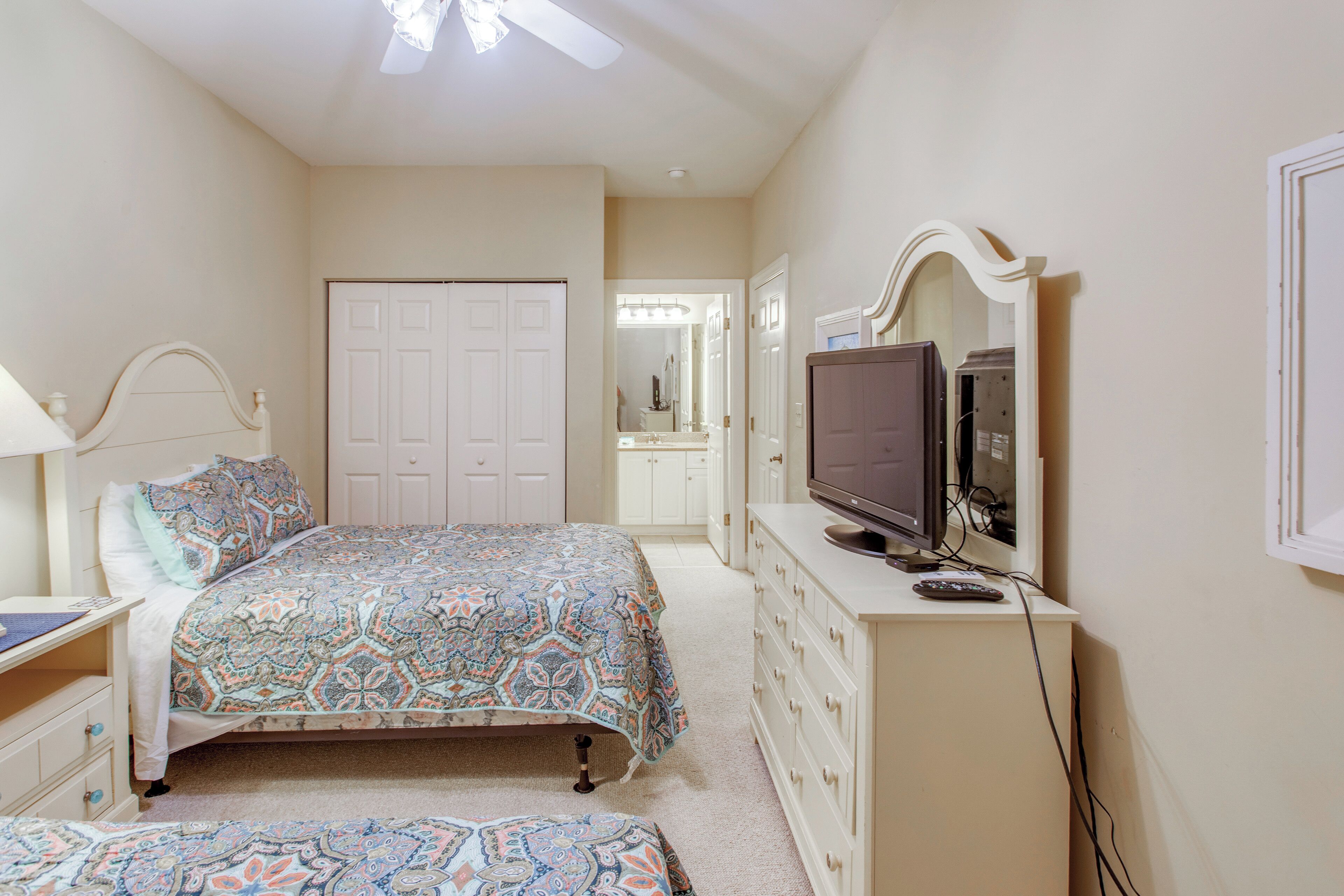 A bedroom with a bed, dresser, television, and a desk.