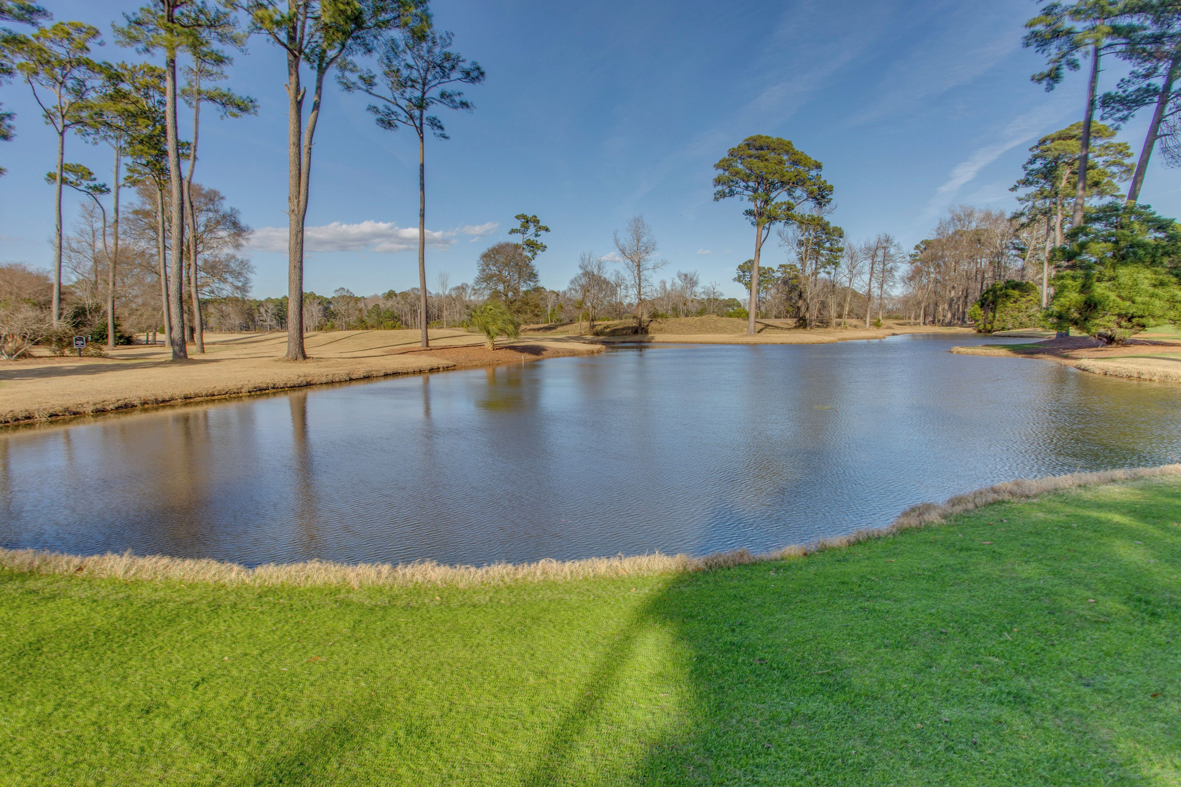 A serene lake with a well-maintained grassy area and tall trees in the background.