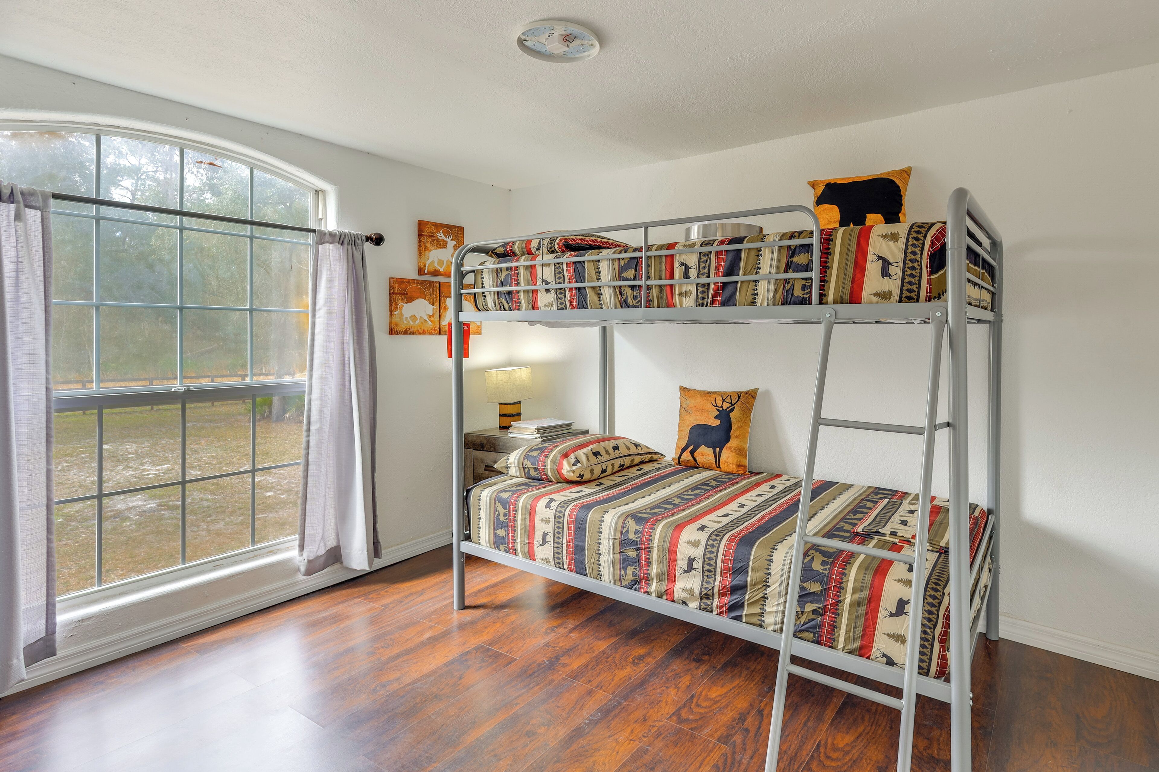 A bunk bed with patterned bedding, a window with curtains, and a view of the outdoors.