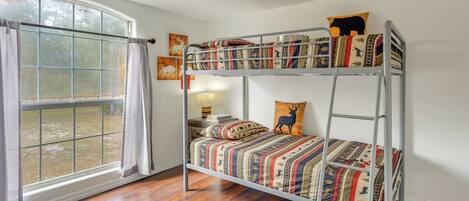 A bunk bed with patterned bedding, a window with curtains, and a view of the outdoors.