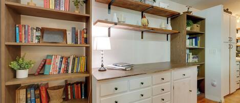 Una habitación con estanterías de madera, un escritorio blanco con cajones y una lámpara.