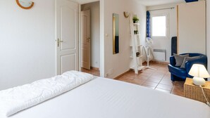 A hotel room with a bed, a chair, a standing fan, a mirror, and a window with curtains. - 3-room villa in Narbonne-Plage, pets allowed (Narbonne-Narbonne Plage-Narbonne Plage)