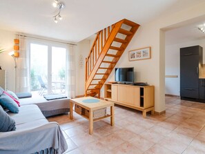 Ein modernes Wohnzimmer mit einer Holztreppe, einem Fernseher auf einem Holzgestell, einer Couch und einem Esstisch.