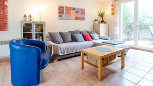 A living room with a sofa, blue armchair, and a wooden coffee table. - 3-room villa in Narbonne-Plage, pets allowed (Narbonne-Narbonne Plage-Narbonne Plage)