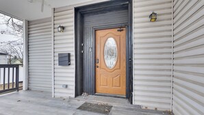 A wooden front door with a glass panel, a mailbox, and two wall-mounted lanterns on a house with horizontal siding. - Explore Nyc, Parks & Beaches! Top-floor Apt (Mount Vernon)
