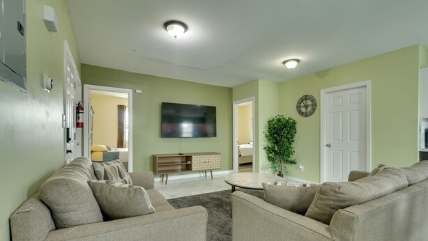 A living room with a beige sofa set, a flat-screen TV mounted on the wall, a small coffee table, and a potted plant. - Explore Nyc, Parks & Beaches! Top-floor Apt (Mount Vernon)