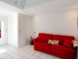 Ein Zimmer mit einem roten Sofa, einem kleinen Tisch mit einer Lampe und einer weißen Tür.