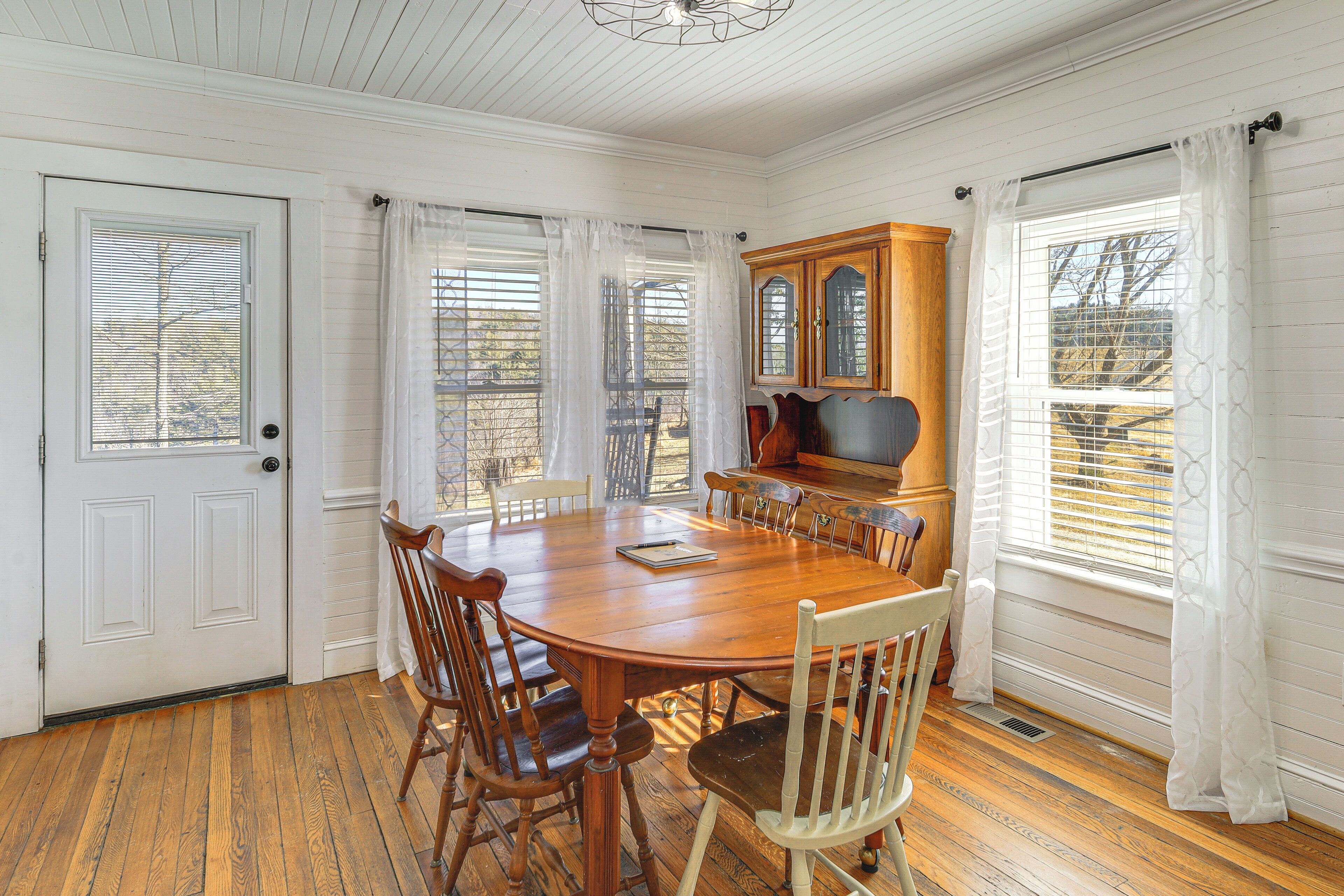 A dining room with a large wooden table surrounded by chairs, a wooden cabinet, and a window with curtains.