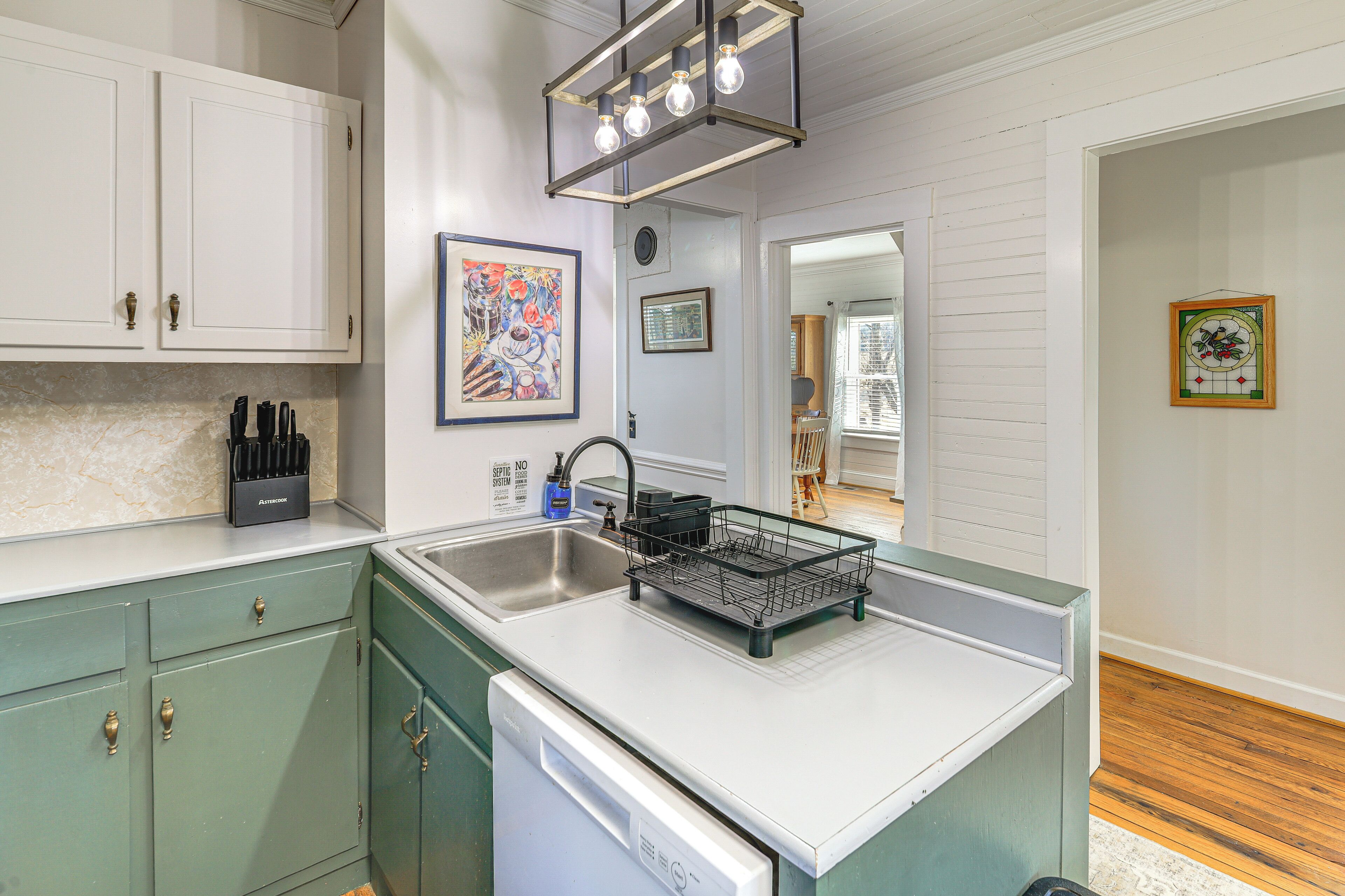 A kitchen with white cabinets, a dishwasher, a sink, and a light fixture above the counter.