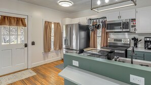 Una cocina moderna con electrodomésticos de acero inoxidable, una isla verde y un ventanal con cortinas.