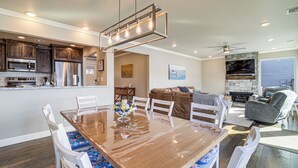 Un vaste espace de vie comprenant une table à manger en bois, des chaises blanches, un canapé gris et une cheminée.