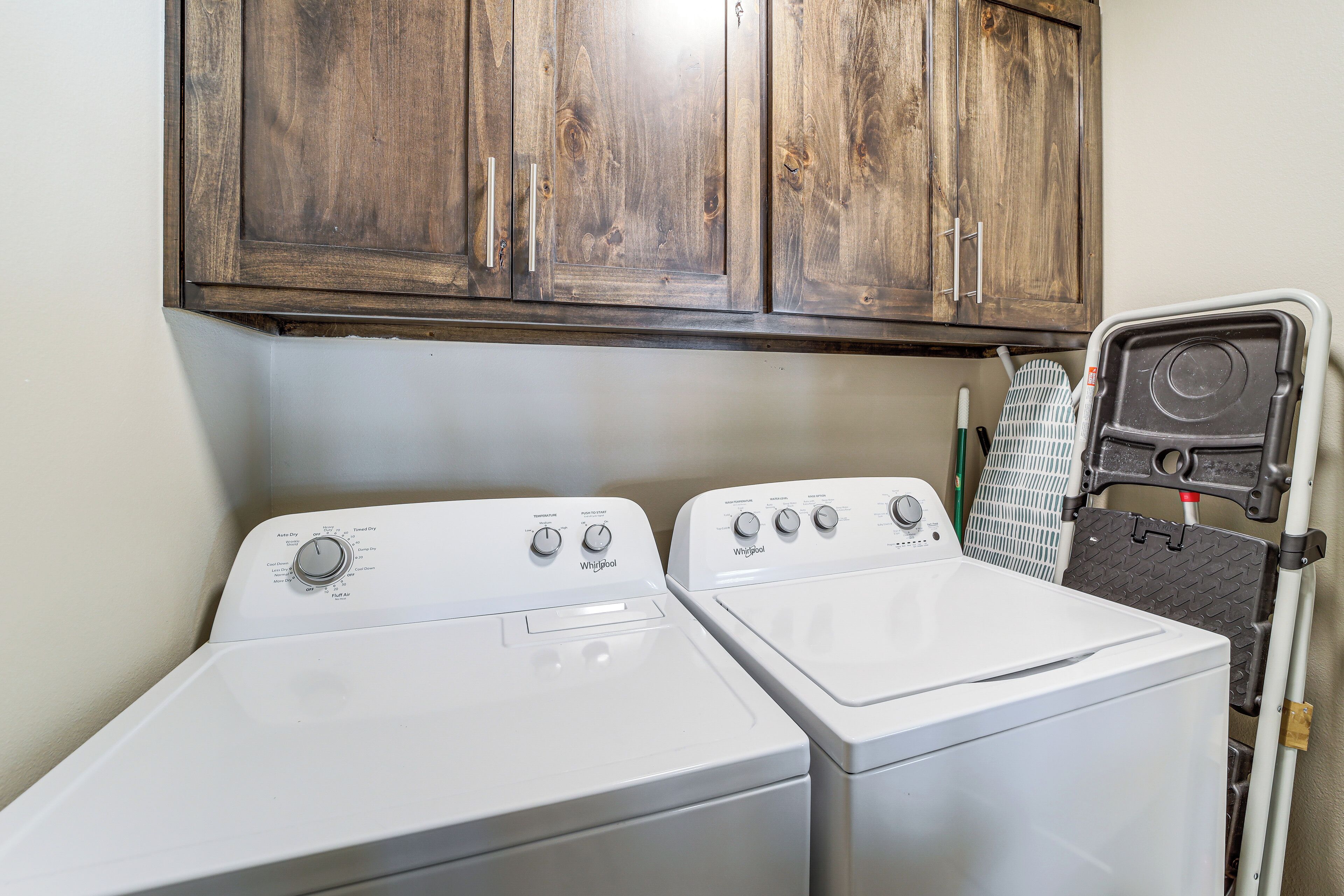 A laundry area with two white front-loading washers and a wooden cabinet above.