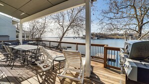Une terrasse extérieure couverte, équipée d’un barbecue, d’une table à manger et de chaises, avec vue sur une étendue d’eau.