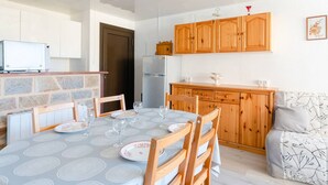 A dining area with a table set for four, wooden cabinets, a refrigerator, and a sofa. - Seaside Apartment in Gruissan with Parking & WiFi Option (Gruissan)