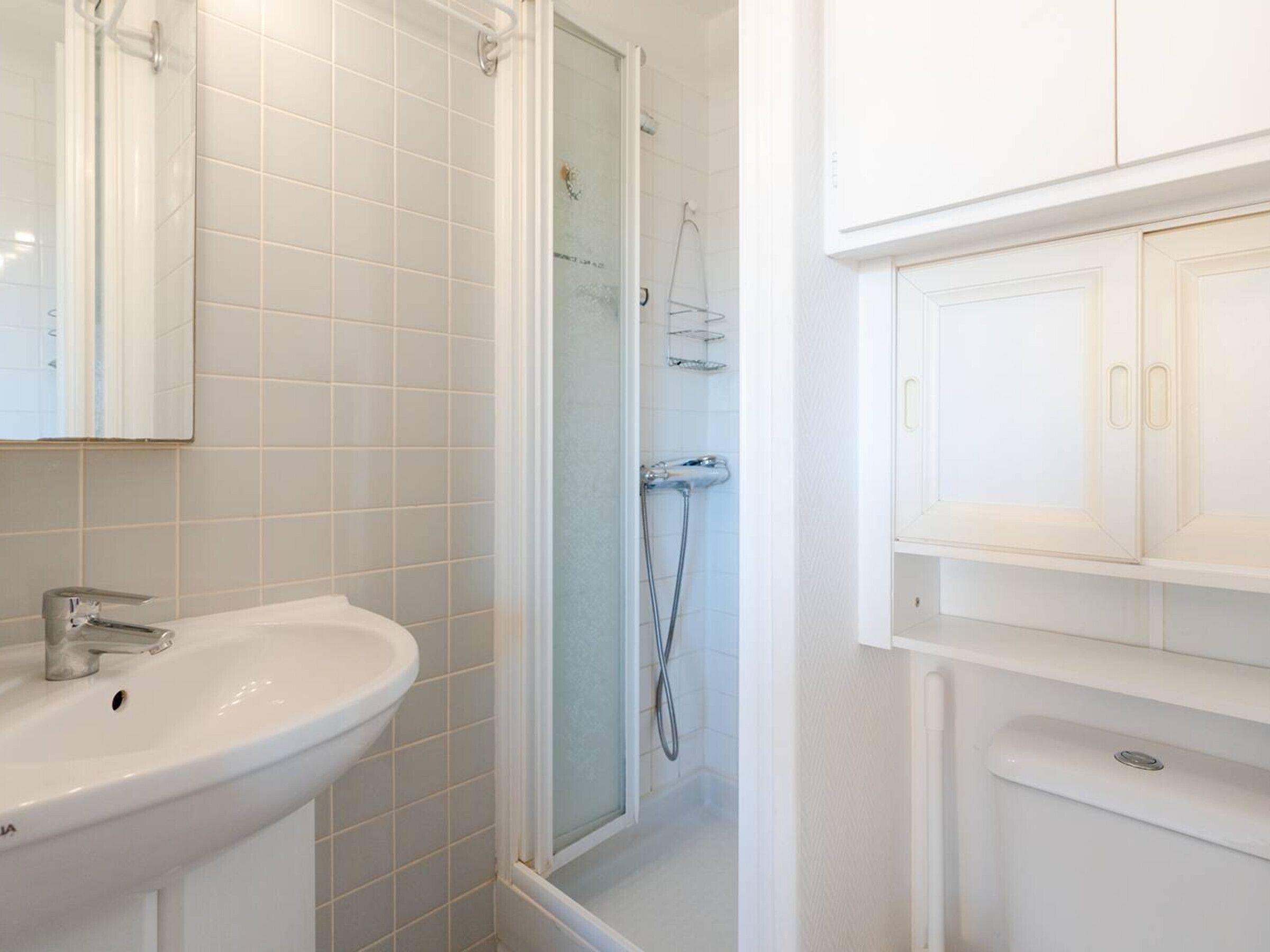 Un bagno con un lavandino bianco, una cabina doccia in vetro e mobili bianchi.