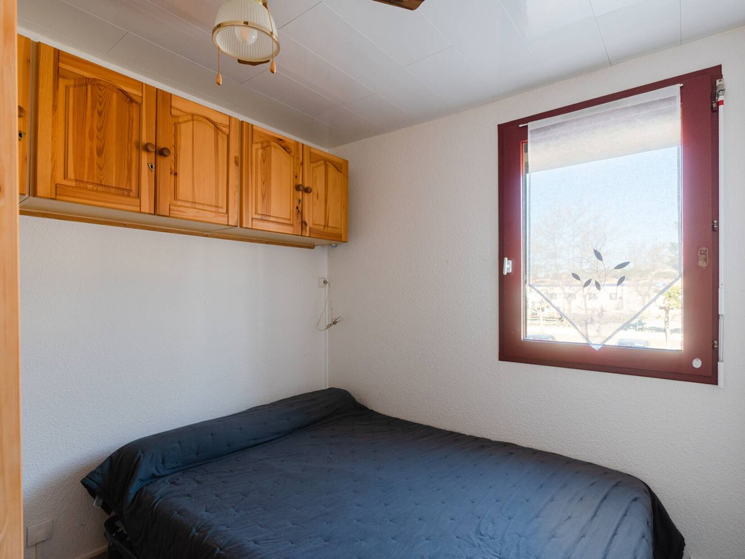 A bedroom with a single bed, wooden cabinets, a window with a view, and a ceiling light fixture.