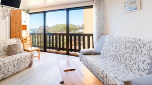 A modern living room with a sofa, a chair, a wooden table, and a TV mounted on the wall. - Seaside Apartment in Gruissan with Parking & WiFi Option (Gruissan)