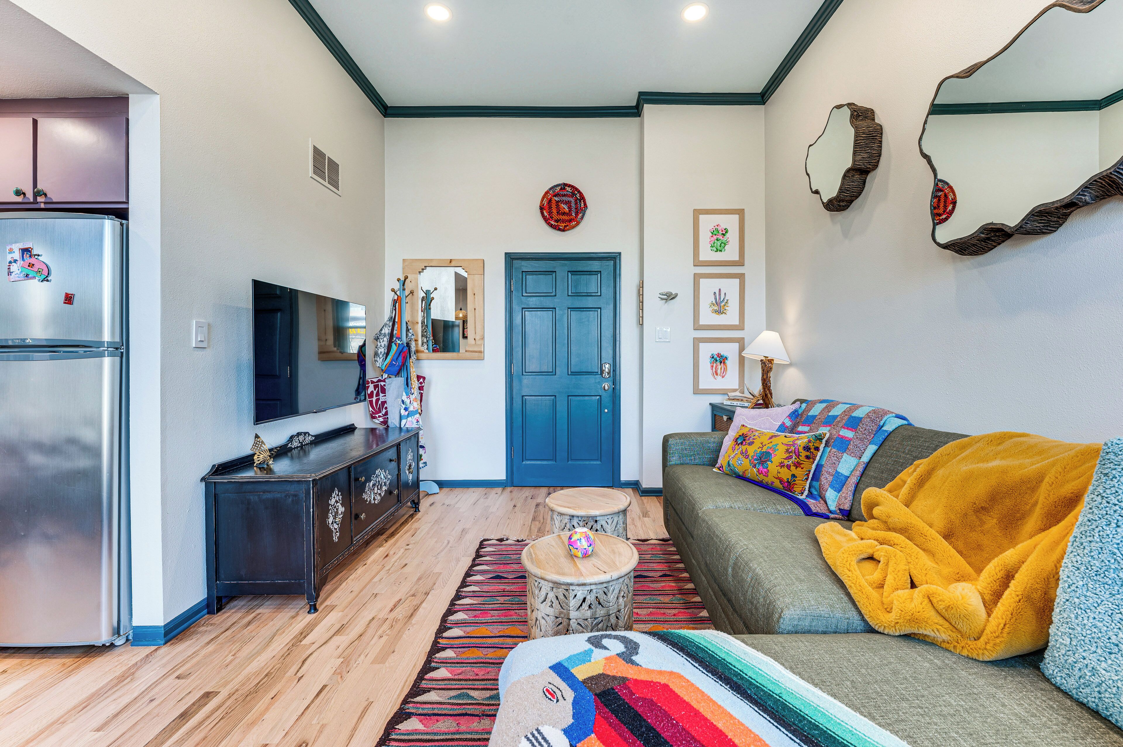 A living room with a sofa, a television, a refrigerator, a wooden cabinet, and a blue door.