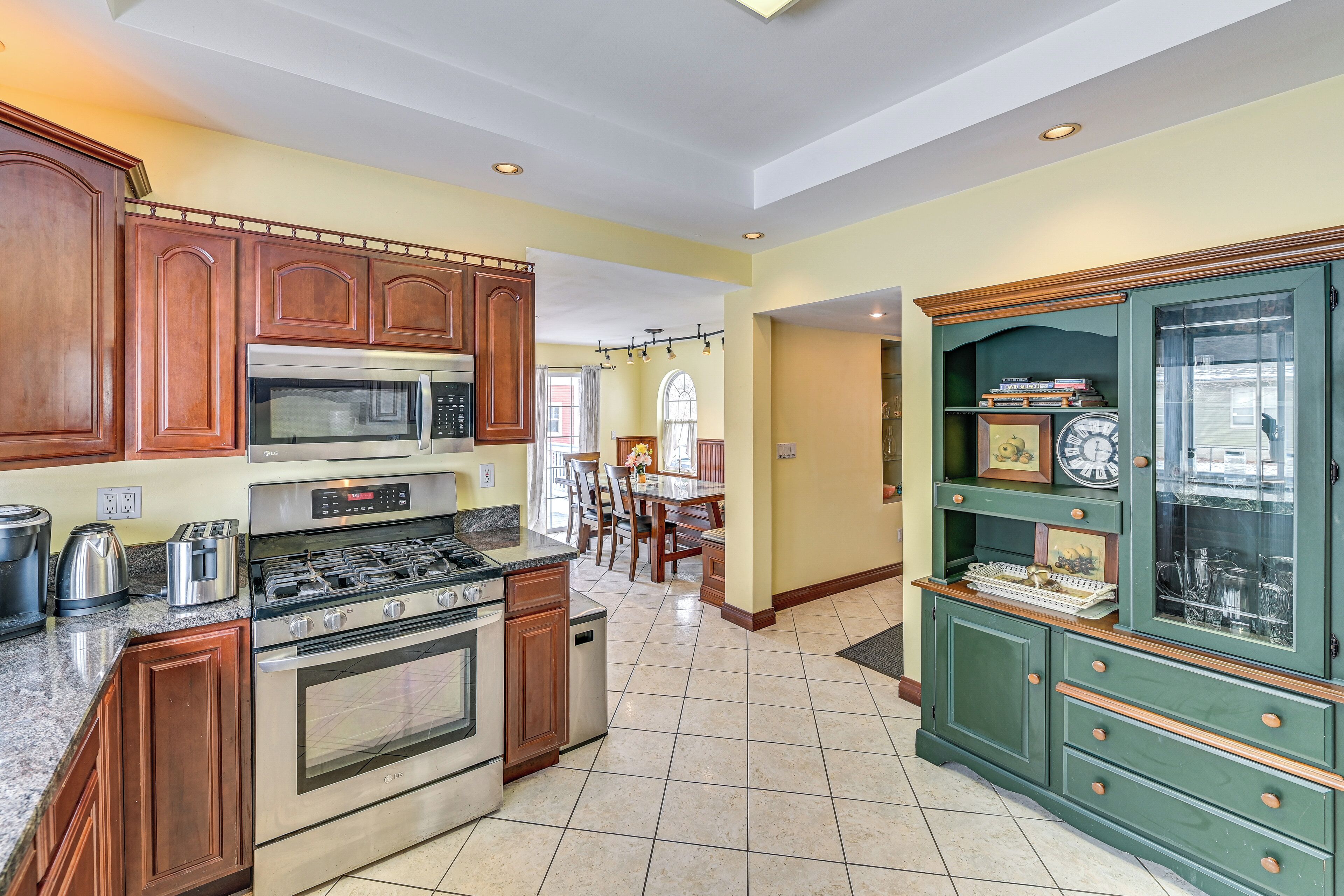 A kitchen with wooden cabinets, a stove, and a microwave. There is a dining area with chairs and a table.