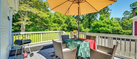 Una terraza con mobiliario de mimbre, una mesa con mantel verde y un paraguas amarillo.