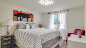 A bedroom with a bed, a nightstand, a lamp, a painting, a window with curtains, and a red chair. - Hike, Golf & Dine: Tucson Retreat w/ Mtn Views! (Tucson)