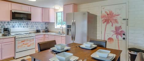 A kitchen with pink cabinets, a stainless steel refrigerator, and a dining table set with bowls and plates.
