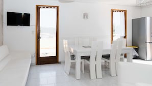 A modern, white-themed living room with a sofa, a dining table with chairs, a TV mounted on the wall, and a refrigerator. - Spacious family villa in Narbonne-Plage for 6 people, private parking, pets allowed (Narbonne-Narbonne Plage-Narbonne Plage)