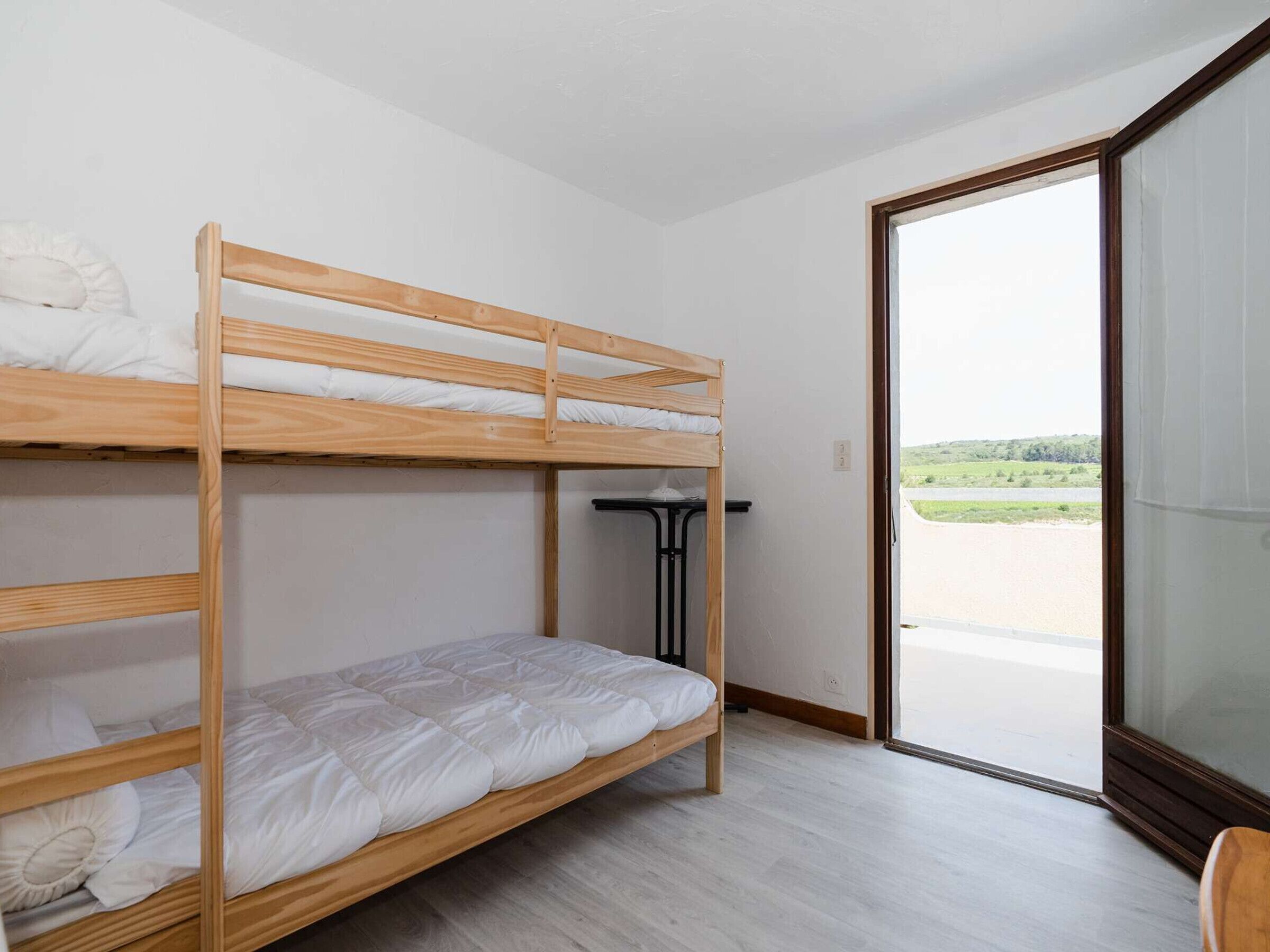 A bunk bed room with a view of a green landscape through a glass door.