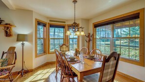 A dining room with a wooden table, chairs, and a chandelier. There are windows with blinds and a sign on the wall. - Mtn-view Cabin w/ Hot Tub Near Blairsville Trails (Blairsville)