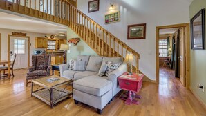 A spacious living room with a wooden staircase, a sofa set, a coffee table, and a kitchen area in the background. - Mtn-view Cabin w/ Hot Tub Near Blairsville Trails (Blairsville)