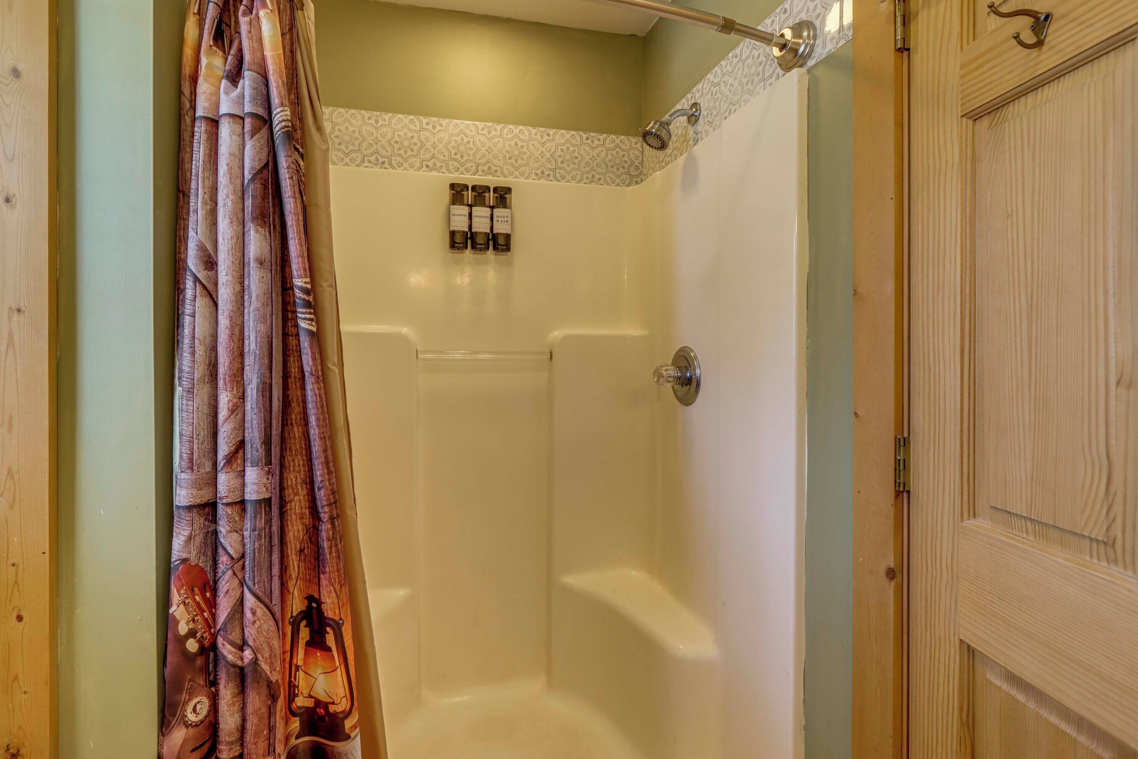 Un espace douche doté d’une porte en bois, d’un rideau de douche au motif rétro et d’un ensemble de produits de toilette fixés au mur.