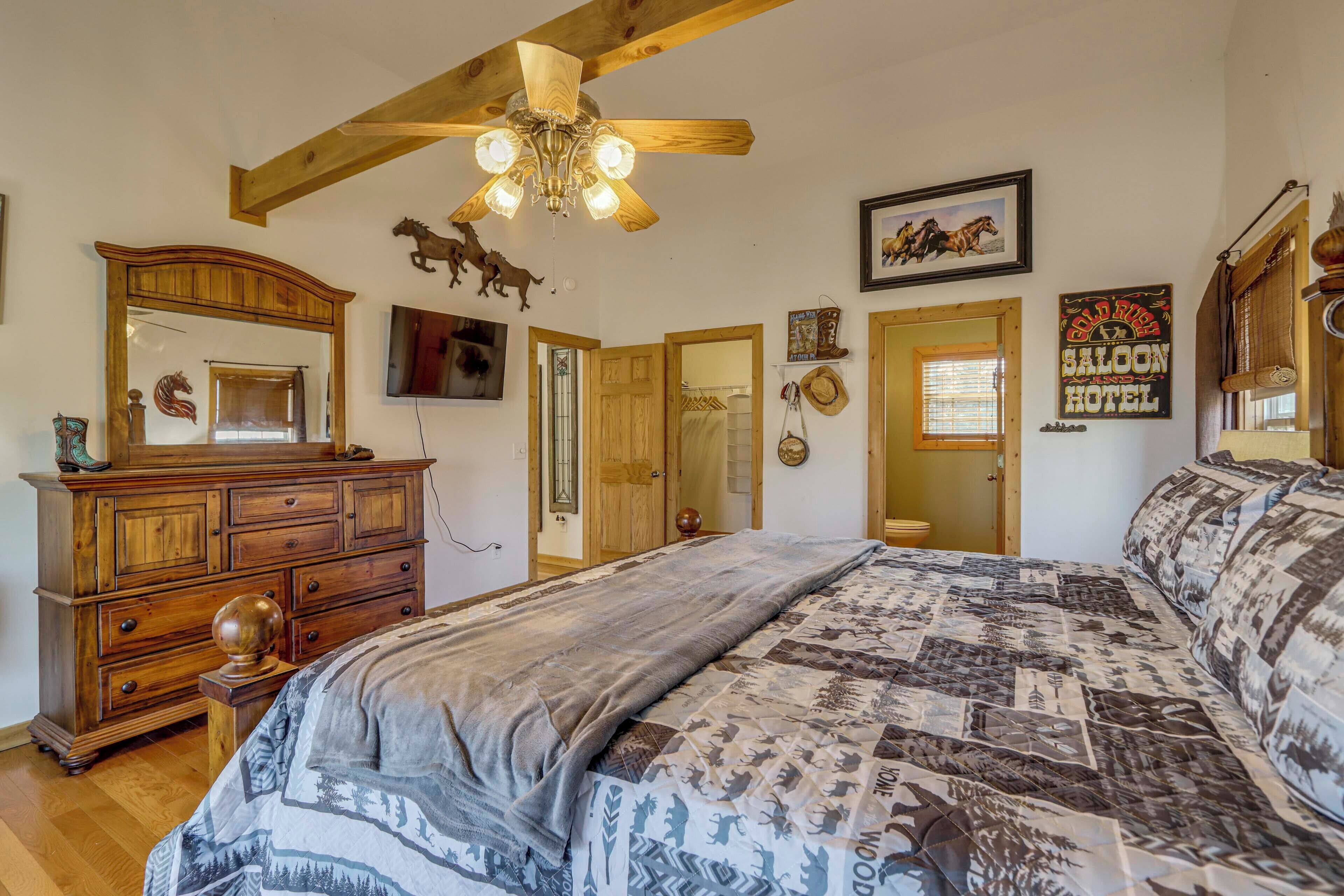A bedroom with a large bed, wooden dresser, ceiling fan, and rustic decor including a sign for the Saloon Hotel.
