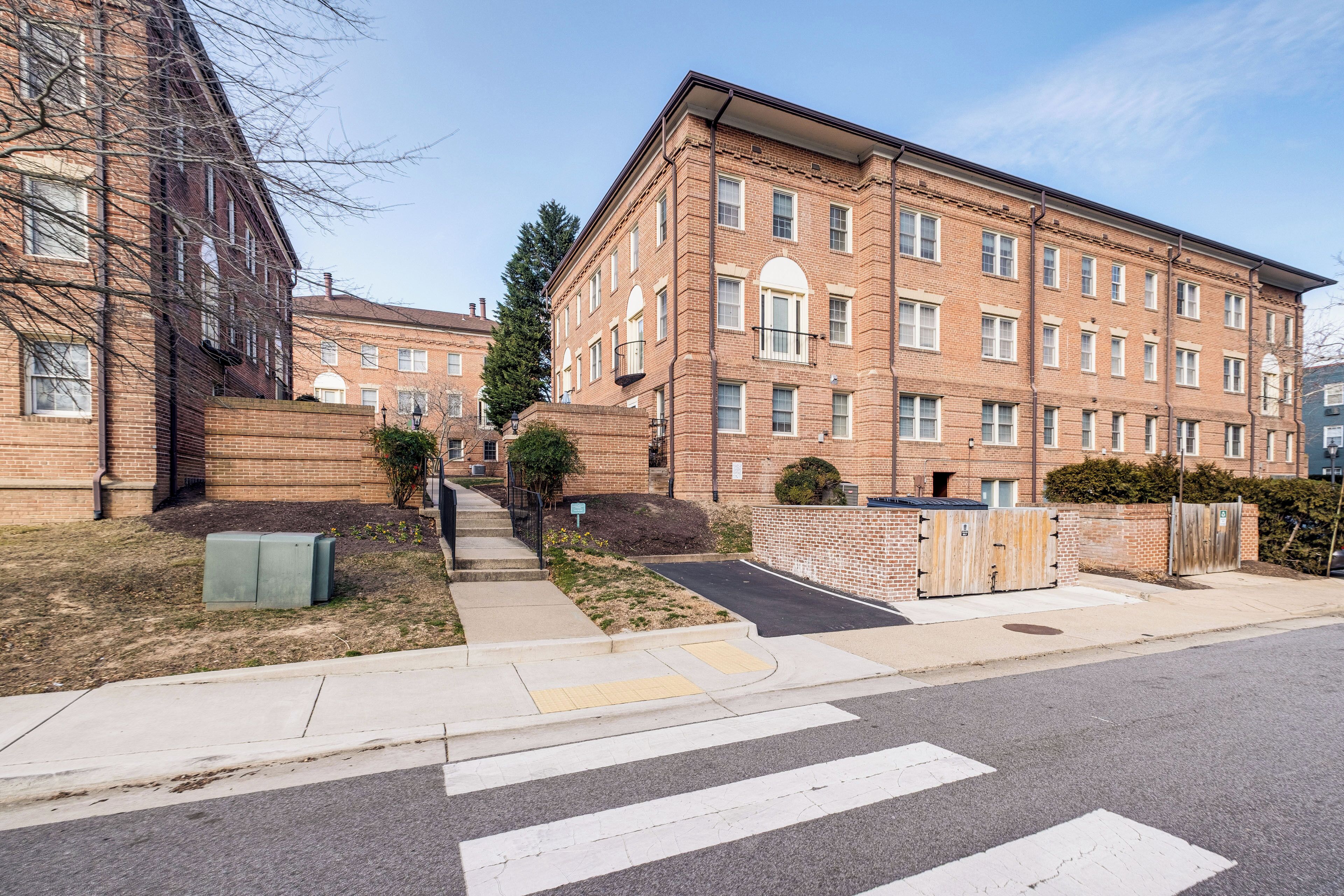 A multi-story brick building with a central courtyard, a crosswalk, and a gated entrance.