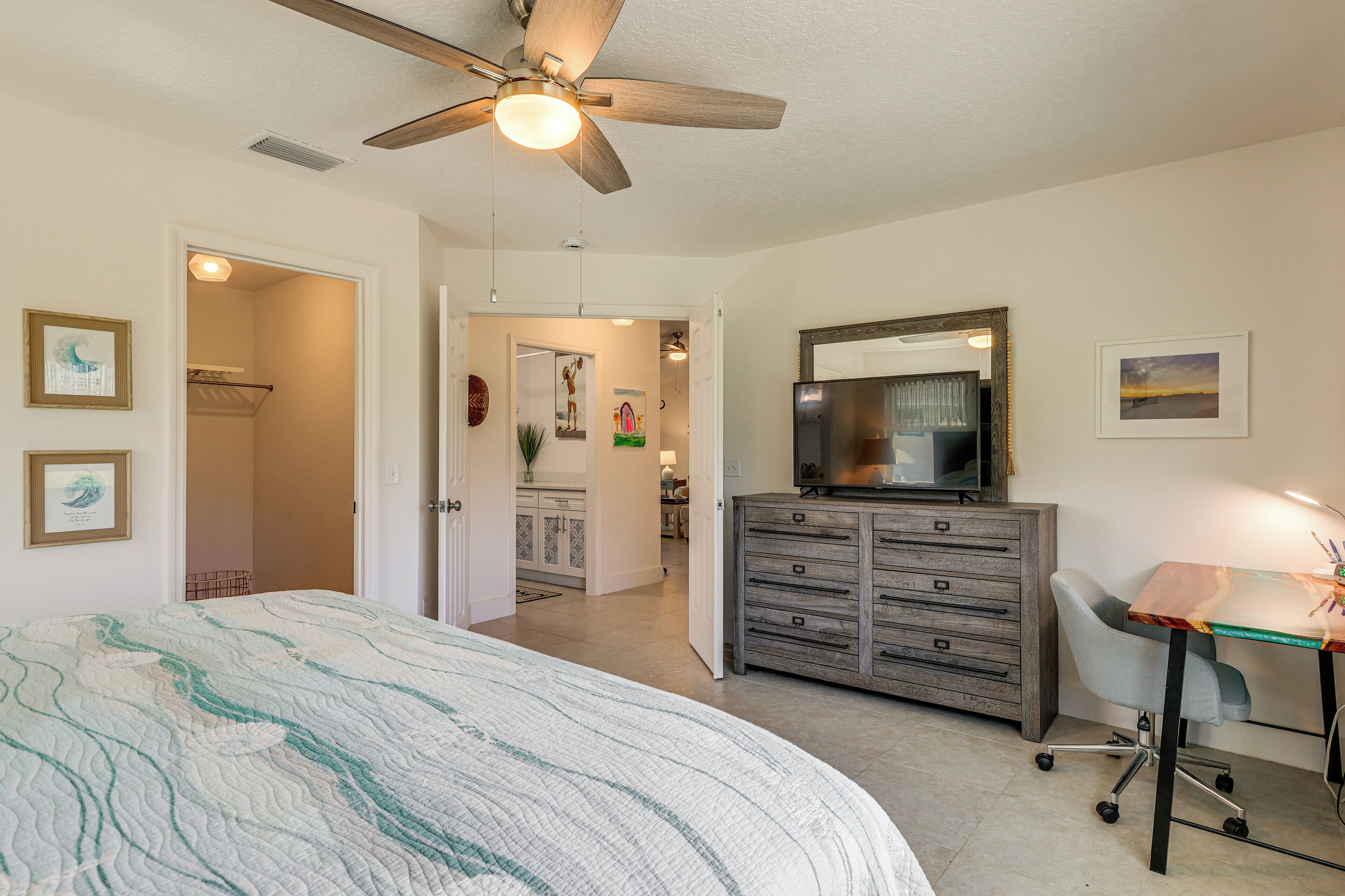 A bedroom with a bed, a dresser, a desk, and a ceiling fan.