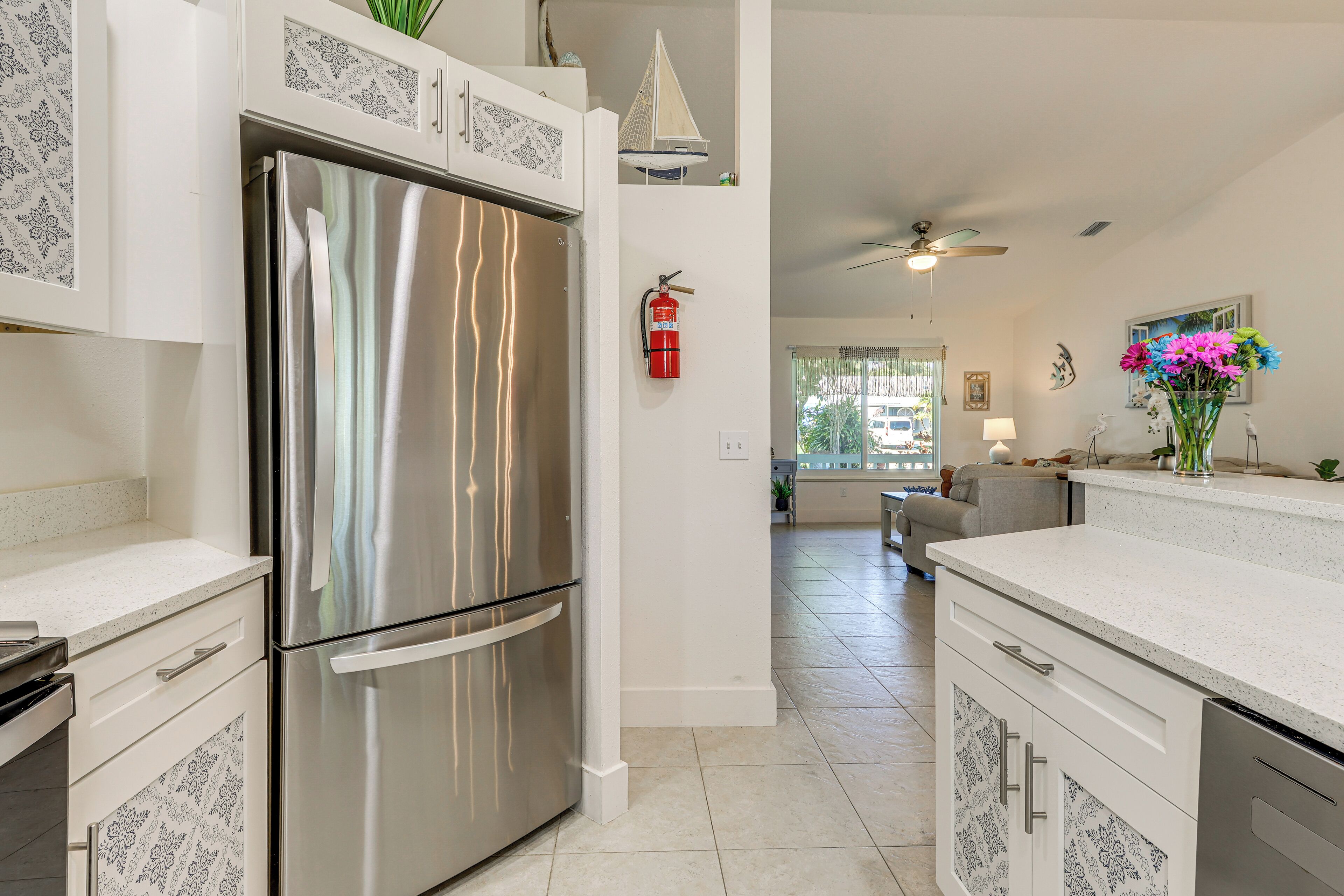 A modern kitchen with a stainless steel refrigerator, white cabinetry, and a ceiling fan.