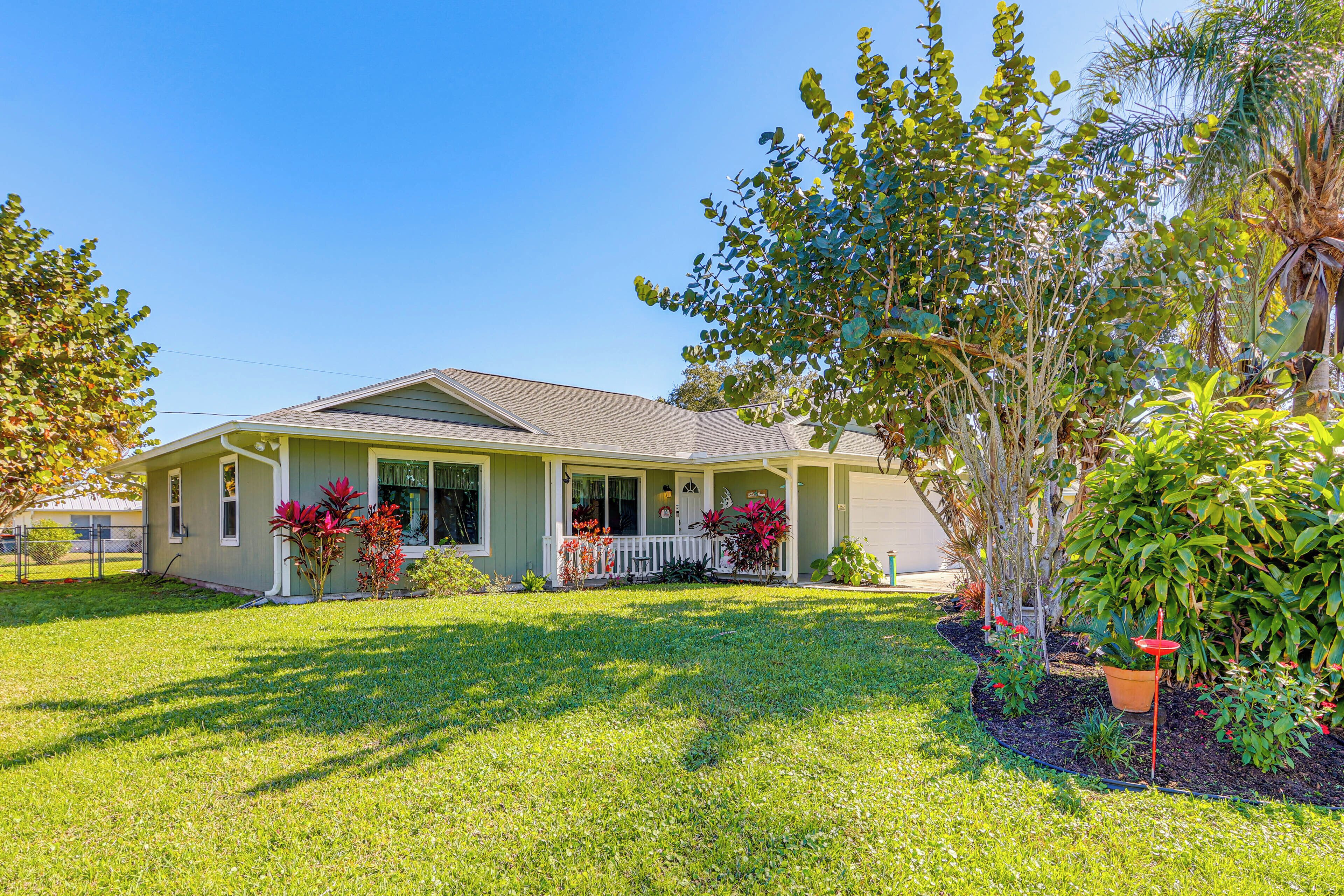 A single-story house with a front porch, surrounded by a well-maintained lawn and various plants.
