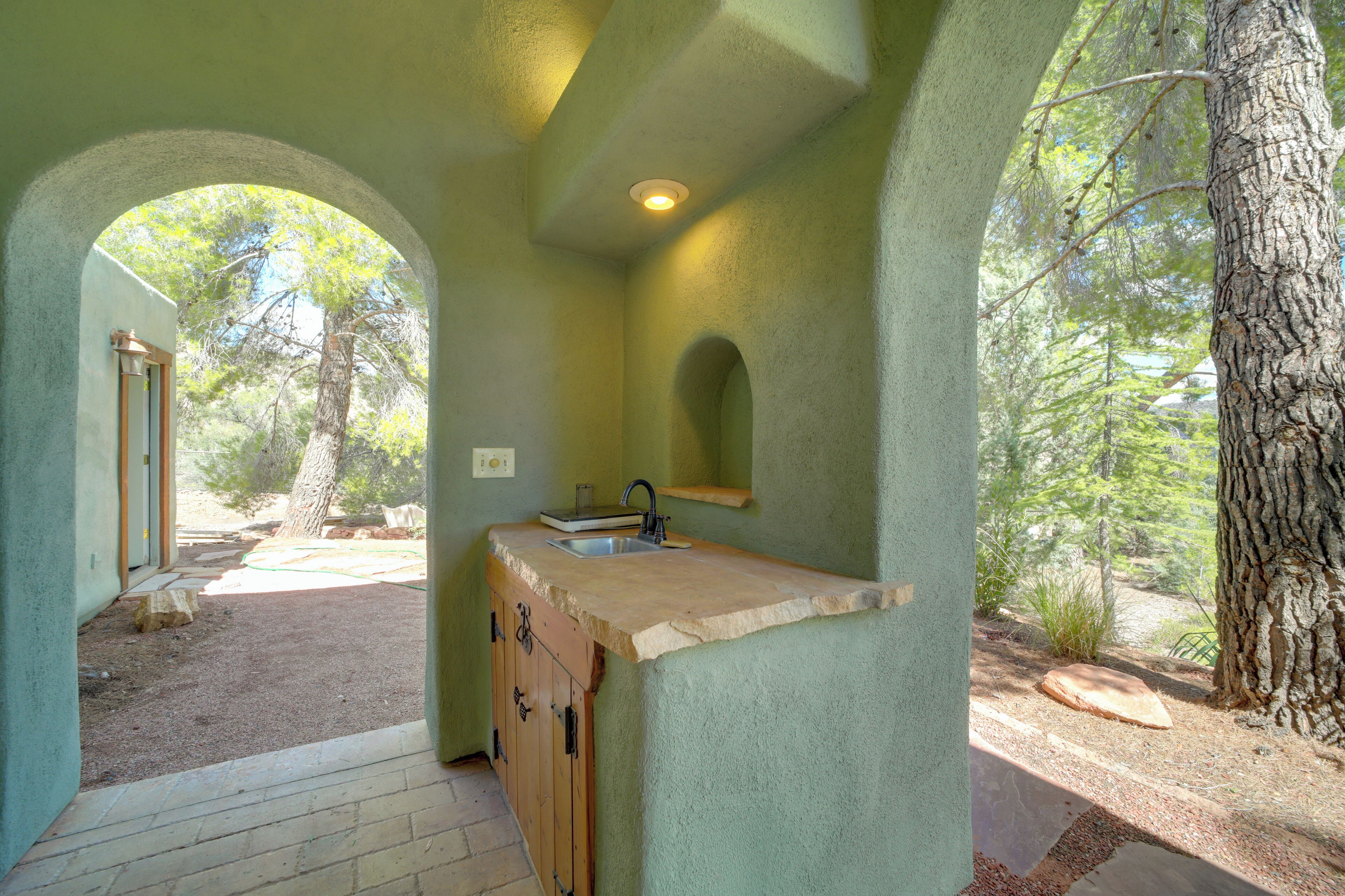 A rustic kitchen with a stone countertop, wooden cabinets, and a view of the surrounding forest.