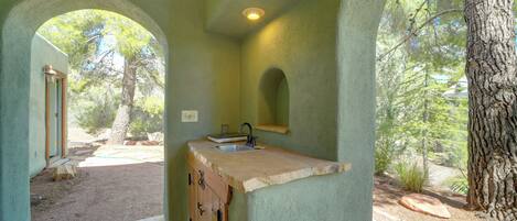 A rustic kitchen with a stone countertop, wooden cabinets, and a view of the surrounding forest.