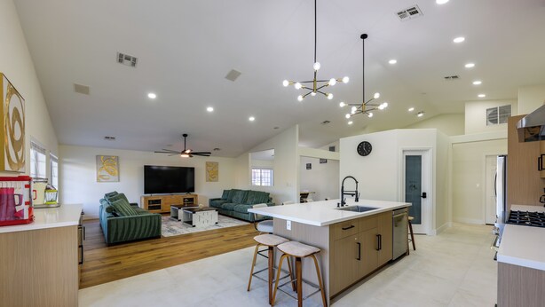 A spacious living area with a large sofa, a TV, and a kitchen island with stools. - Patio w/ Fairway View! Pet-friendly Mohave Home (Fort Mohave)
