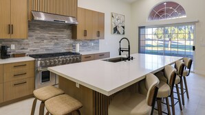 A modern kitchen with a large island, stainless steel appliances, and a view of a golf course through a large window. - Patio w/ Fairway View! Pet-friendly Mohave Home (Fort Mohave)