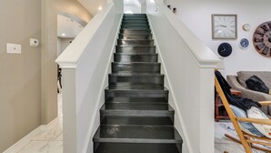 A staircase with a white handrail and black steps, leading to a landing with a ceiling fan and a wall clock. - 3 Mi to Randolph Afb: San Antonio Area Home (Universal City)