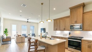 A modern kitchen with wooden cabinets, a central island with bar stools, a built-in oven, and pendant lighting. - 4 Mi to NRG Stadium: Modern Group Retreat (Houston)