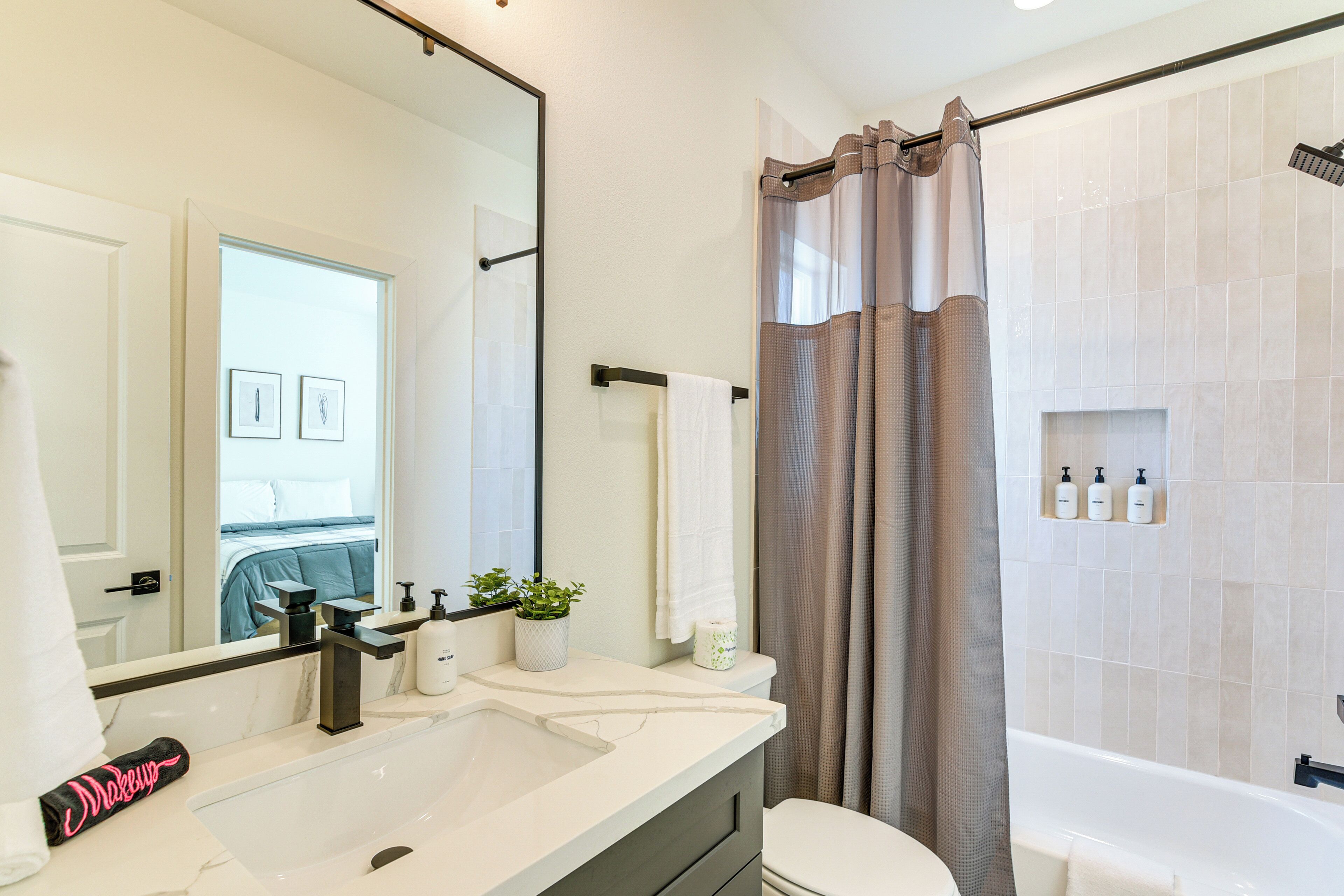 A modern bathroom with a large mirror, a sink, a toilet, and a bathtub.