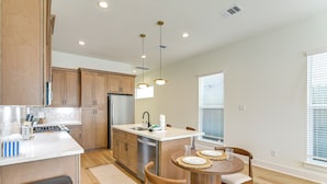 A modern kitchen with wooden cabinets, a stainless steel refrigerator, and a dining area with a round table and chairs. - 4 Mi to NRG Stadium: Modern Group Retreat (Houston)