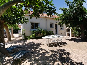 A patio with a table and chairs, a brick wall, and a building with a tiled roof. - Renovated house near the sea with air conditioning and WIFI (Fleury-Saint-Pierre-la-Mer)