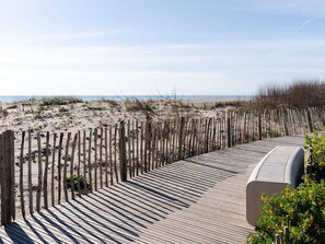 A wooden boardwalk leading to a beach with a sandy landscape and sparse vegetation. - Renovated house near the sea with air conditioning and WIFI (Fleury-Saint-Pierre-la-Mer)